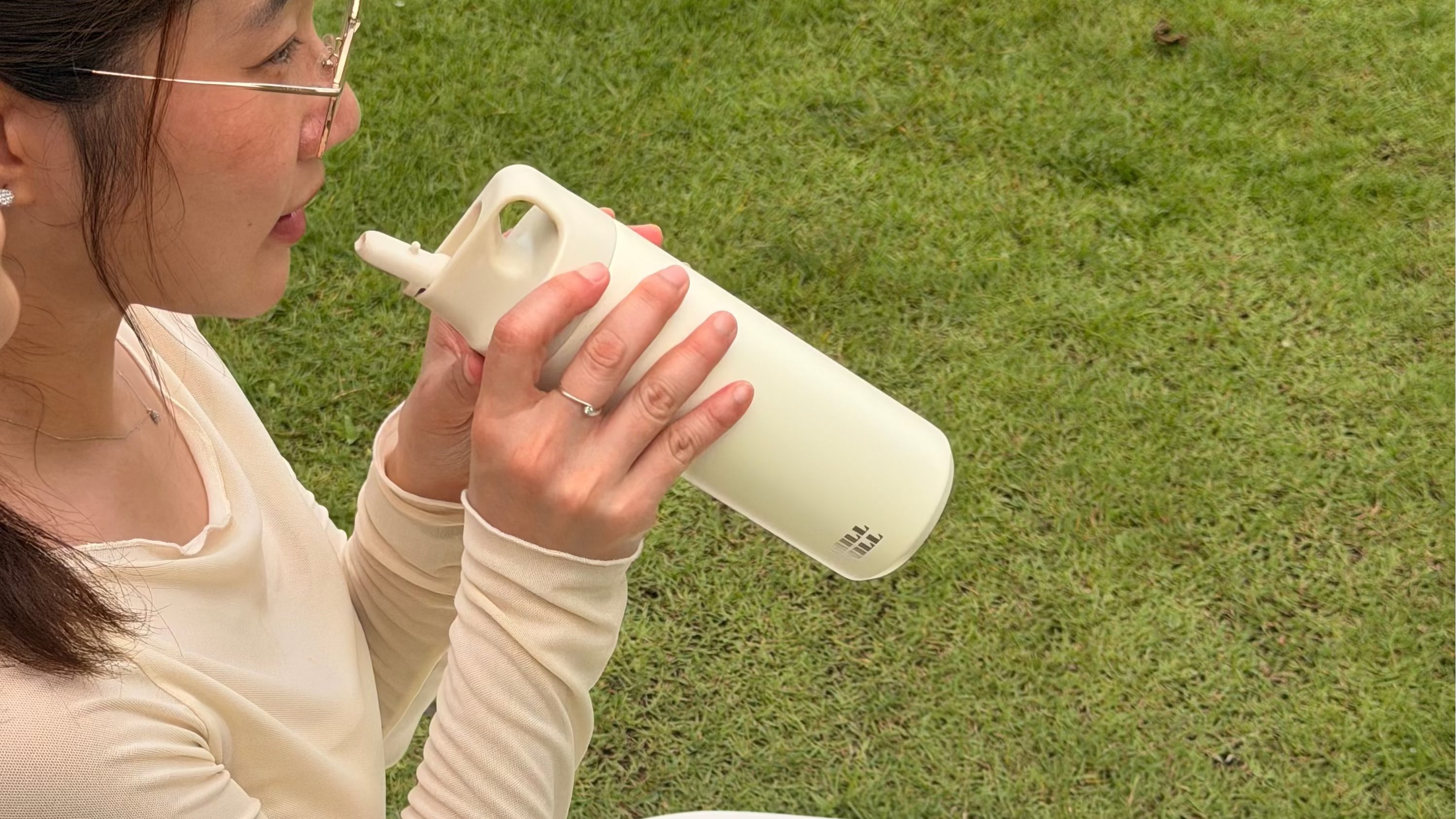 Woman sitting on a white mat outdoors, holding a white water bottle.
